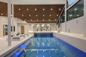 A modern indoor swimming pool with a minimalist design, a wooden ceiling, and a large window providing a view of the outdoors. - Lemmer Estate - Tarzana Golf Course Home with Indoor Pool (Tarzana)