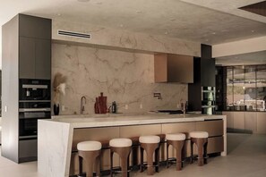 A modern kitchen with a marble backsplash, built-in appliances, and bar stools. - Lemmer Estate - Tarzana Golf Course Home with Indoor Pool (Tarzana)