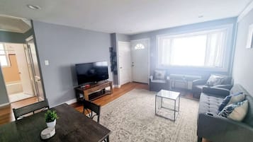 A living room with a flat-screen TV, a sofa, a coffee table, and a dining table with chairs.