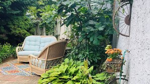 A garden area with a wicker chair, a metal planter with flowers, and a wall-mounted planter with orange flowers. - Inviting 1BR Apartment — Rockledge Location (Rockledge)