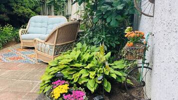 A garden area with a wicker chair, a metal planter with flowers, and a wall-mounted planter with orange flowers.