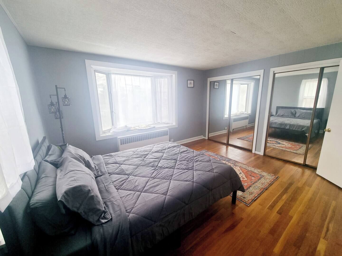 A bedroom with a bed, a radiator, a window, and a sliding door leading to another room.