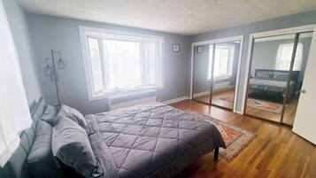 A bedroom with a bed, a radiator, a window, and a sliding door leading to another room.