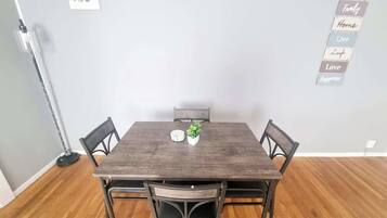 A dining area with a wooden table and four chairs, a small potted plant, and a wall-mounted sign with positive phrases.