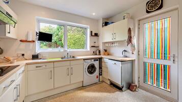 A modern kitchen with a built-in washing machine, a window with a view of greenery, and a colorful striped door.