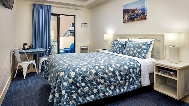 A hotel room with a bed, bedside tables, a desk with chairs, a ceiling fan, and a painting on the wall. - 2 Units | Seaport Village Stay Avalon Waterfront Views (Avalon)