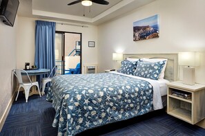 Hotellihuone, jossa on sänky, yöpöydät, työpöytä tuoleineen, kattotuuletin ja taulu seinällä.