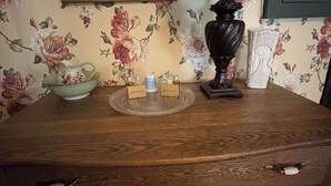 A wooden dresser with three drawers, a lamp, and a floral wallpaper. - Grand Victorian - Easy GAP Access, shops, and restaurants (Confluence)