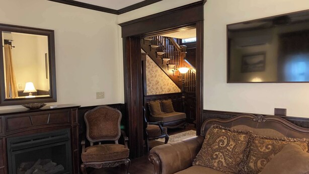 A living room with a fireplace, a sofa, a chair, and a staircase leading to an upper level. - Grand Victorian - Easy GAP Access, shops, and restaurants (Confluence)