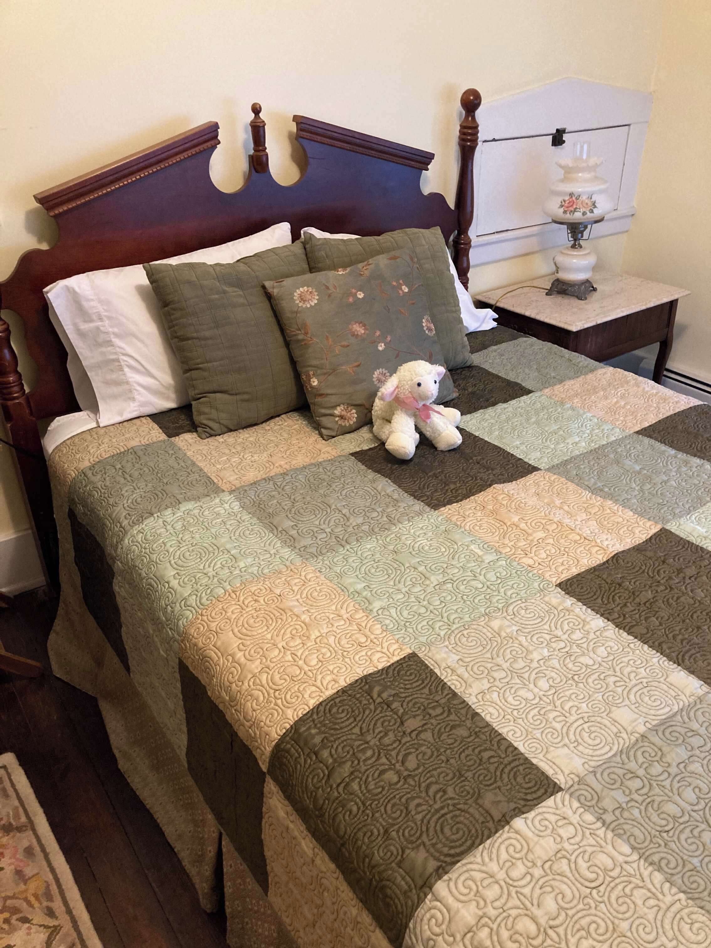 A bed with a quilt, pillows, and a stuffed toy.
