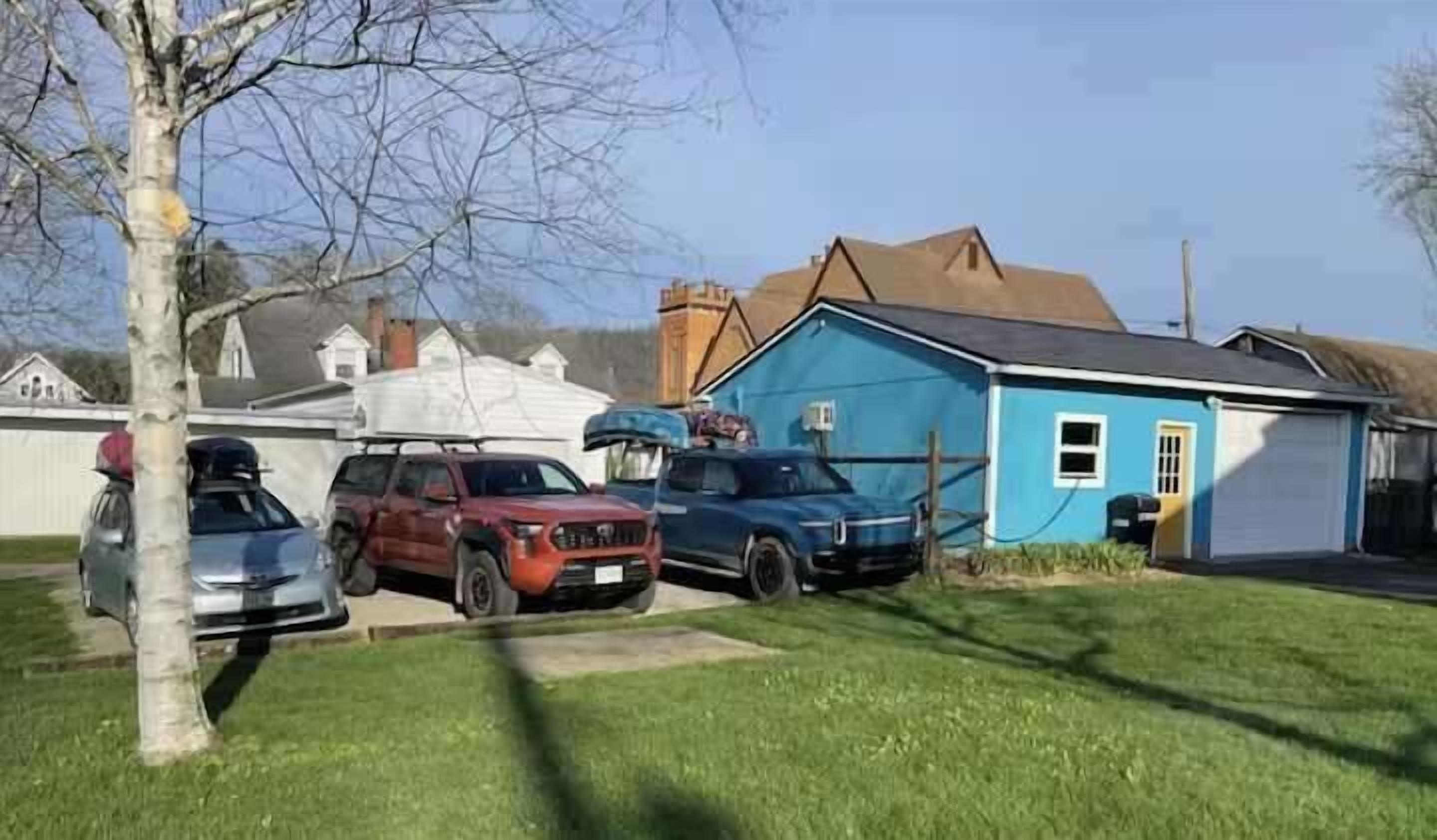 Un barrio residencial con una casa azul, un garaje y tres coches estacionados.
