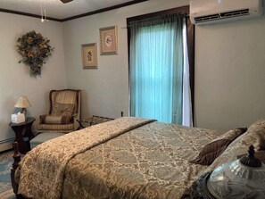 Quarto de hotel com uma cama grande, uma cadeira, um abajur e uma janela com cortinas.