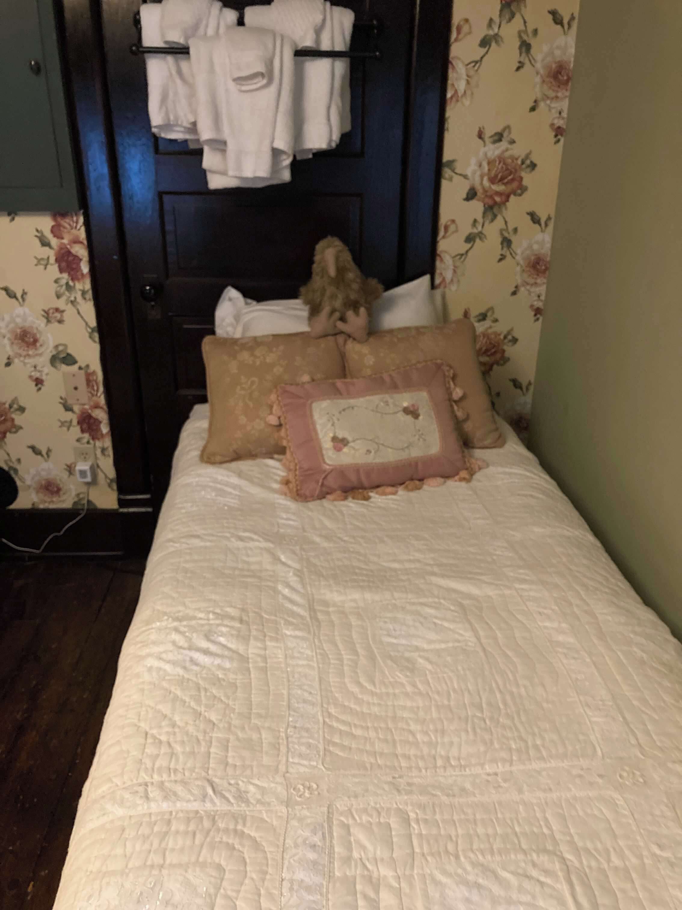 Una cama con cubrecolcha acolchado, dos almohadas y un peluche pequeño.