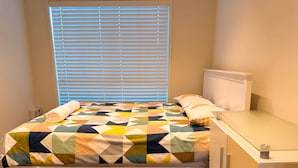 A bed with a geometric-patterned quilt, a bedside table, and a window with blinds. - Bluewater Sanctuary: Luxury Beach house with private jetty (Tascott)