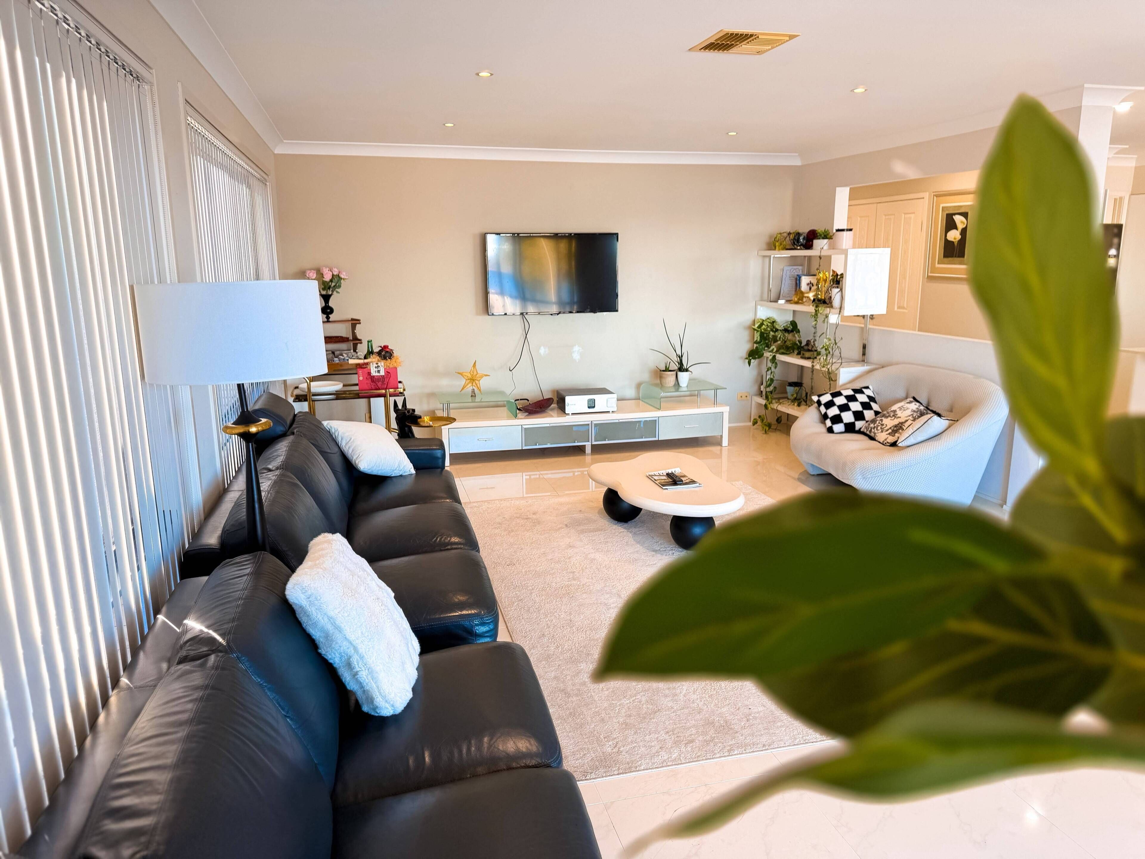 A modern living room with a black leather sofa, a glass coffee table, and a flat-screen TV mounted on the wall.