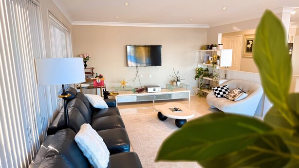 A modern living room with a black leather sofa, a glass coffee table, and a flat-screen TV mounted on the wall. - Bluewater Sanctuary: Luxury Beach house with private jetty (Tascott)