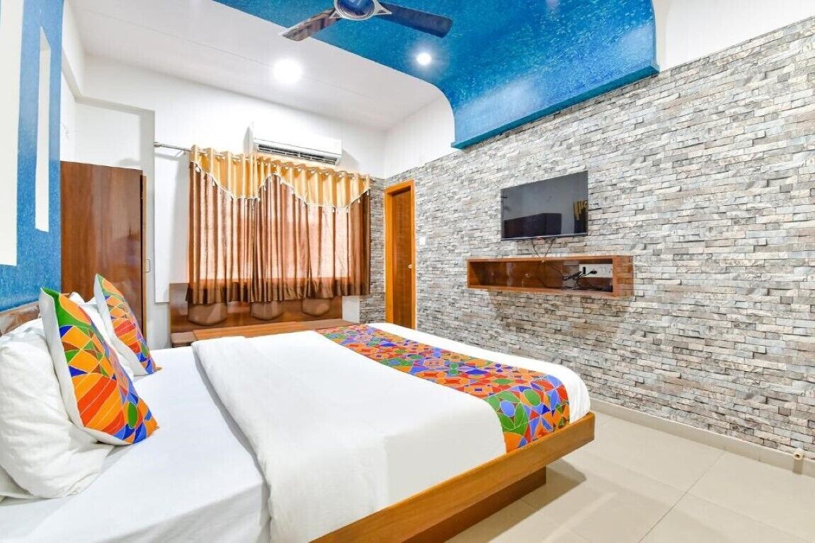 A hotel room with a bed, a flat-screen TV mounted on the wall, and a ceiling fan.