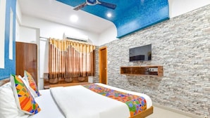 A hotel room with a bed, a flat-screen TV mounted on the wall, and a ceiling fan. - Hotel Meet Residency (Ahmedabad)