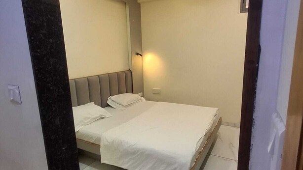 A bedroom with a bed, a ceiling fan, and a wall-mounted light fixture. - Hotel Meet Residency (Ahmedabad)