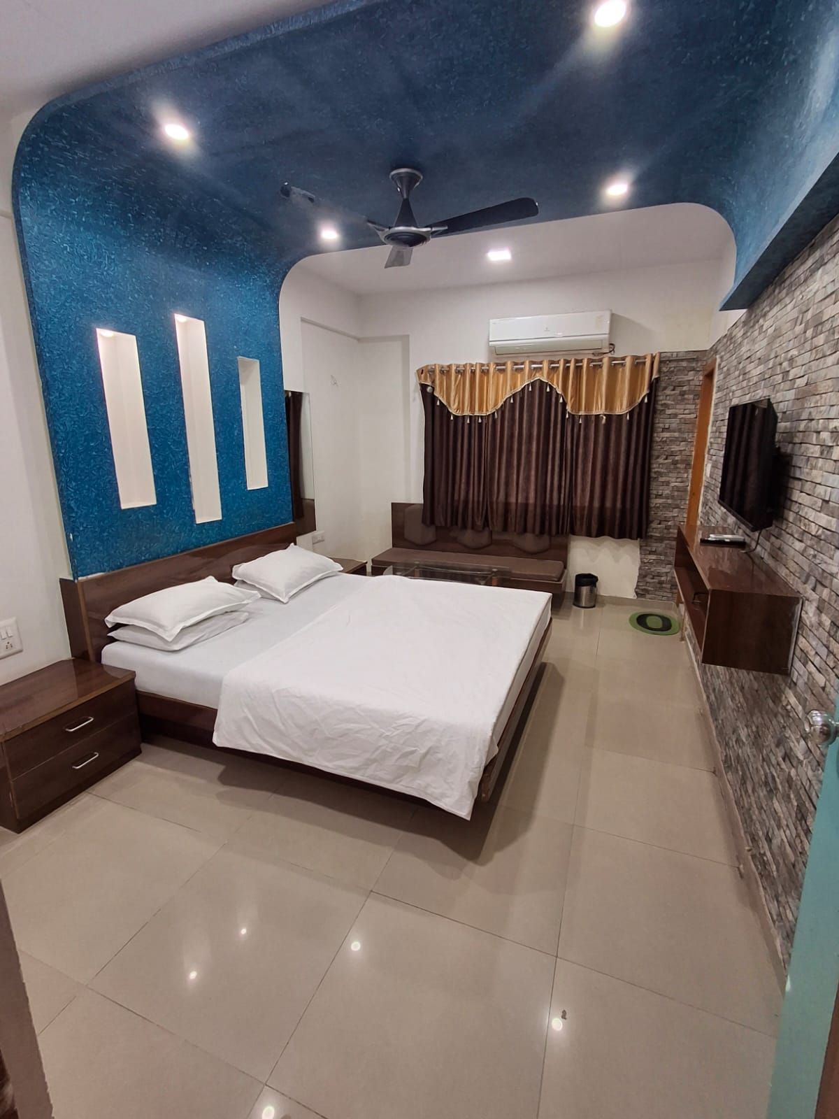 A bedroom with a bed, bedside tables, a ceiling fan, and a TV mounted on the wall.
