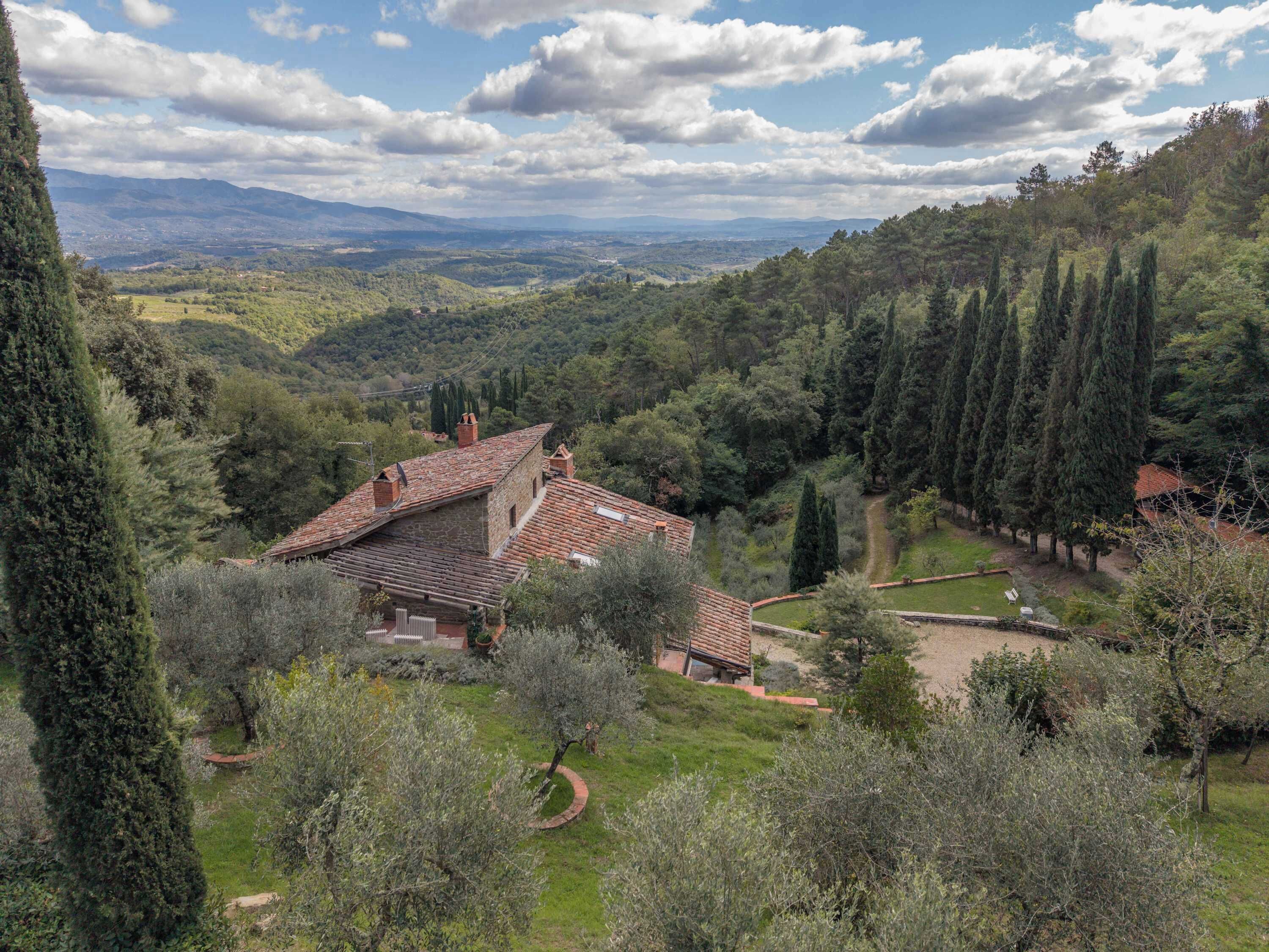 A villa with a tiled roof, surrounded by olive trees and a hilly landscape.