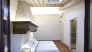 Ein kleiner, abgeschlossener Raum mit einem Bett, einer Dusche und einer Tür zu einem weiteren Raum.