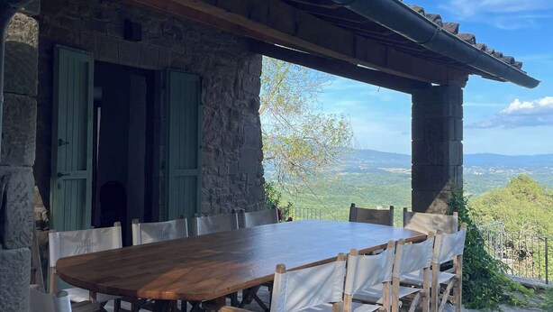 Ein Gebäude aus Stein mit einem Holztisch und -stühlen, einem überdachten Außenbereich und Blick auf die Landschaft.
