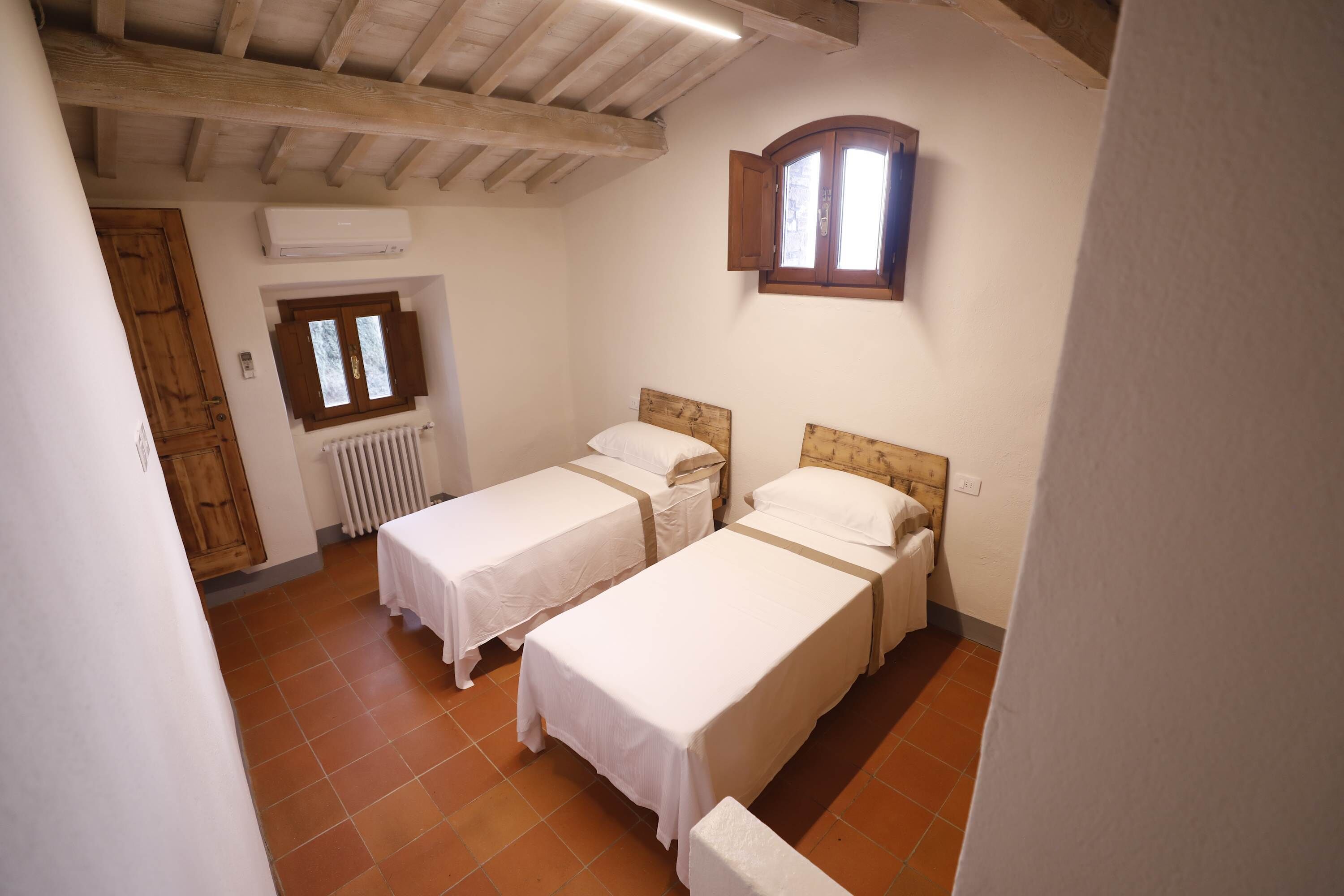 A room with two single beds, a radiator, a window, and a wooden door.