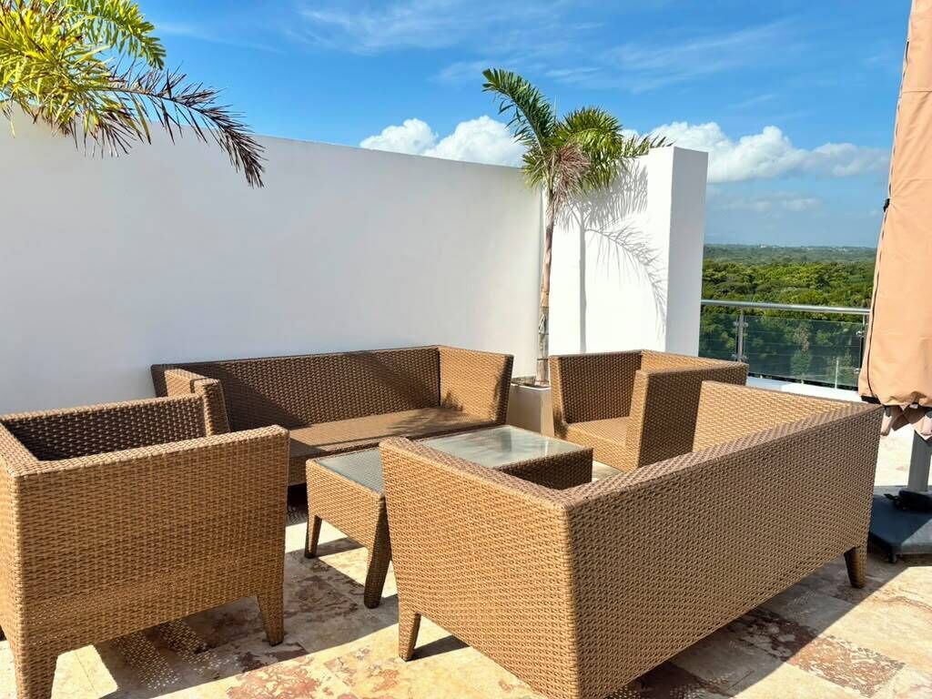 Un balcon agrémenté de meubles en osier, d’une table à plateau en verre et offrant une vue sur le paysage.
