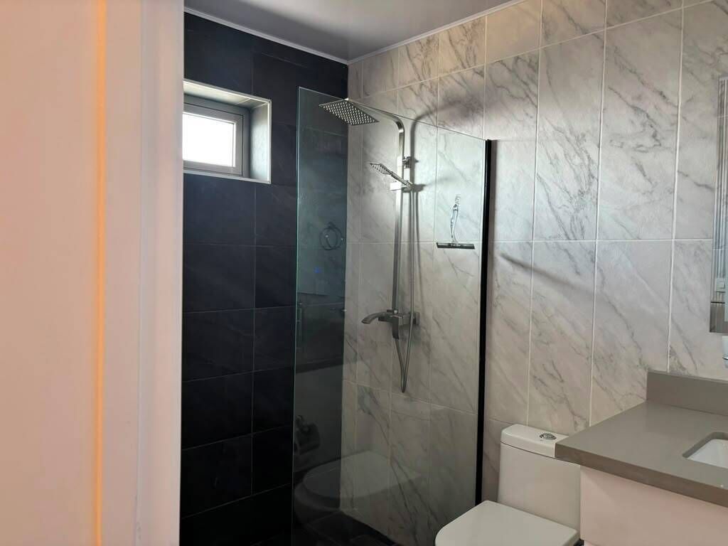 Une salle de bain moderne avec une douche à parois de verre, des toilettes et un mur recouvert de carreaux de marbre.