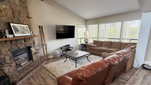 En stue med en pejs af sten, en stor lædersofa, et fladskærms-tv og en stenvæg som detalje.