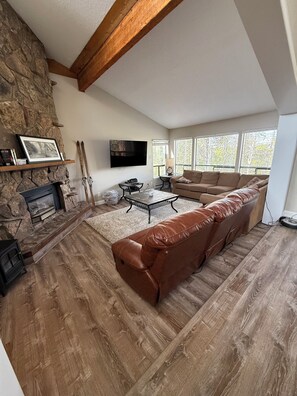A living room with a stone fireplace, a large leather sofa, a flat-screen TV, and a stone accent wall. - Beautiful 3 Bedroom/2.5 bath Condo Steps from Downtown Winter Park (Winter Park)