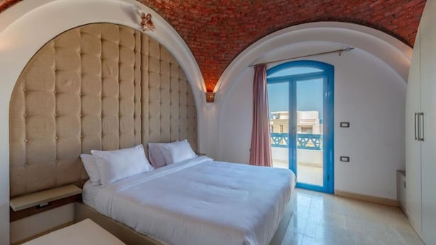 A bedroom with a large bed, a bench, and a view of the outside through a blue door. - Spacious villa with private pool (Red Sea Governorate)