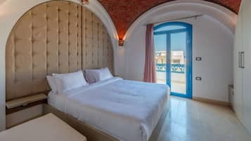 Ein Schlafzimmer mit einem großen Bett, einer Bank und Blick durch eine blaue Tür nach draußen.