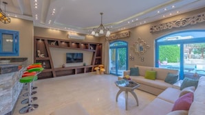 A modern living room with a large sofa, a TV, and a bar area with stools. - Spacious villa with private pool (Red Sea Governorate)