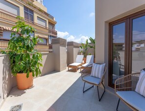 A balcony with two wicker chairs, a potted plant, and a tiled floor.