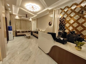 A modern hotel lobby with a reception desk, seating area, and a decorative wall. - SHRI KHATUSHYAM RESIDENCY (Varanasi)