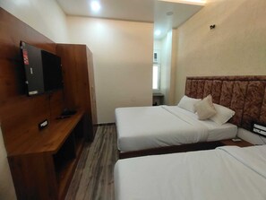 A hotel room with two beds, a TV mounted on a wooden panel, and a window with an air conditioning unit. - SHRI KHATUSHYAM RESIDENCY (Varanasi)