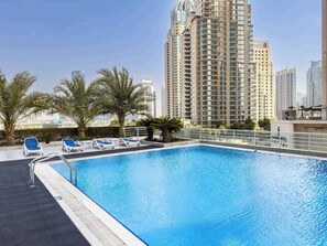 A rooftop swimming pool with lounge chairs and palm trees, surrounded by high-rise buildings. - Free Housekeeping Visits During Your Stay - Stayshort - Bright 1 Bedroom Retreat in Dubai Marina That Sleeps 2 (Dubai)