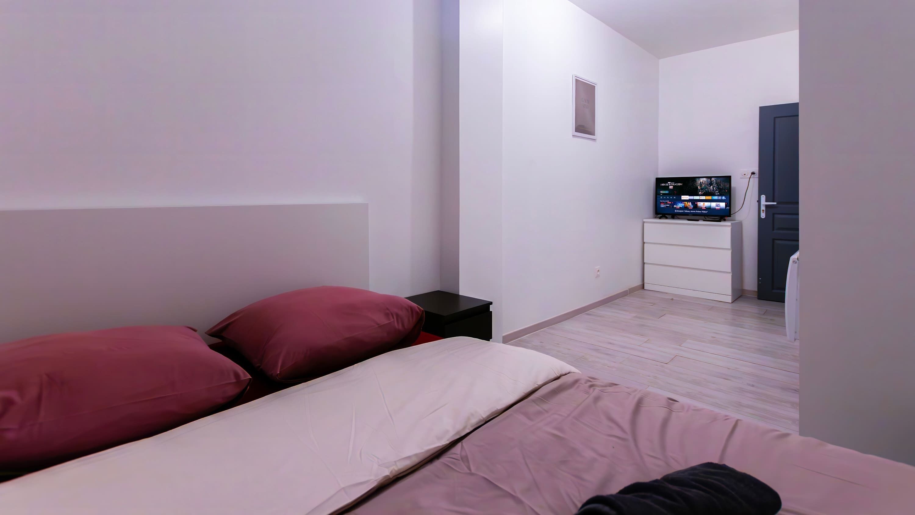 A bedroom with a bed, pillows, a nightstand, a TV, and a dresser.