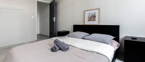 A bedroom with a bed, a nightstand, a bedside table, a door, and a framed picture on the wall.