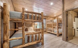 A cabin interior with bunk beds made of wood, a wooden door, and a window with blinds. - Luxury 12BR Smoky Mtn. Cabin/ Sleeps 34/ Indoor Pool/ Hot tub/ Theater (Pigeon Forge)