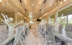 A wooden interior with a long dining table, chairs, and decorative plants. - Luxury 12BR Smoky Mtn. Cabin/ Sleeps 34/ Indoor Pool/ Hot tub/ Theater (Pigeon Forge)
