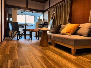A modern living room with a sofa, a coffee table, and a dining area with chairs. - MSTAY Oshiage One (Sumida-ku)