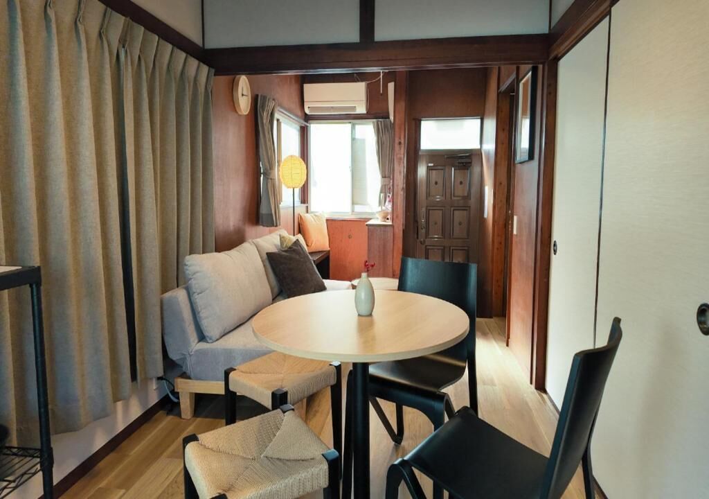 A cozy room with a round table, a sofa, and a chair. There is a clock on the wall and a lamp on a side table.