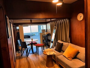 Ein gemütlicher Wohnbereich mit einer Couch, einem Tisch, einem Sessel, einem großen Spiegel und Blick auf eine Küche und einen Balkon.