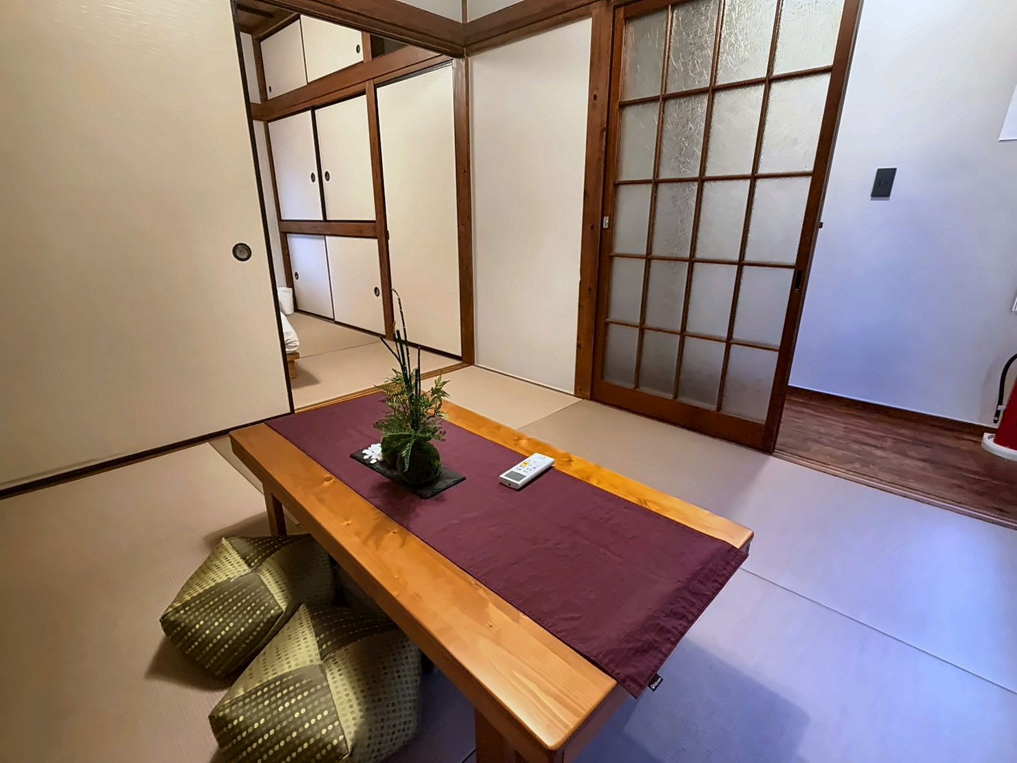 A tatami mat room with a wooden table, cushions, and a shoji screen door.