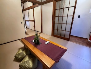Ein Raum mit Tatami-Matten, einem Holztisch, Kissen und einer Shoji-Schiebetür.