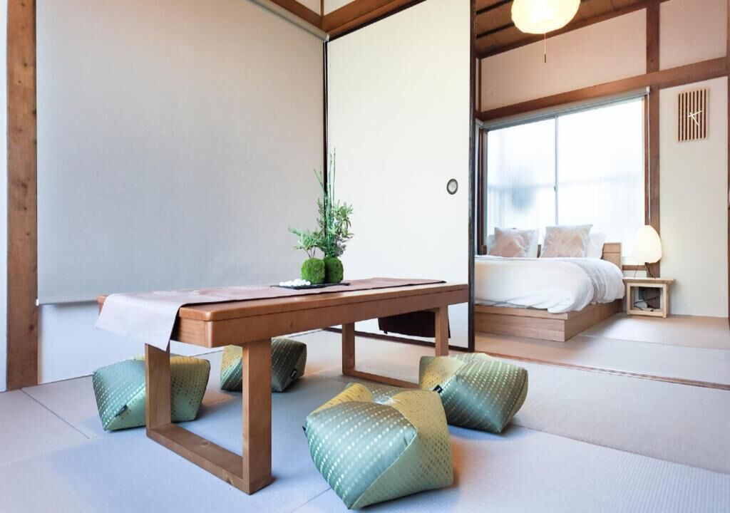 A traditional Japanese-style room with tatami flooring, a low wooden table, and a bed with white bedding.