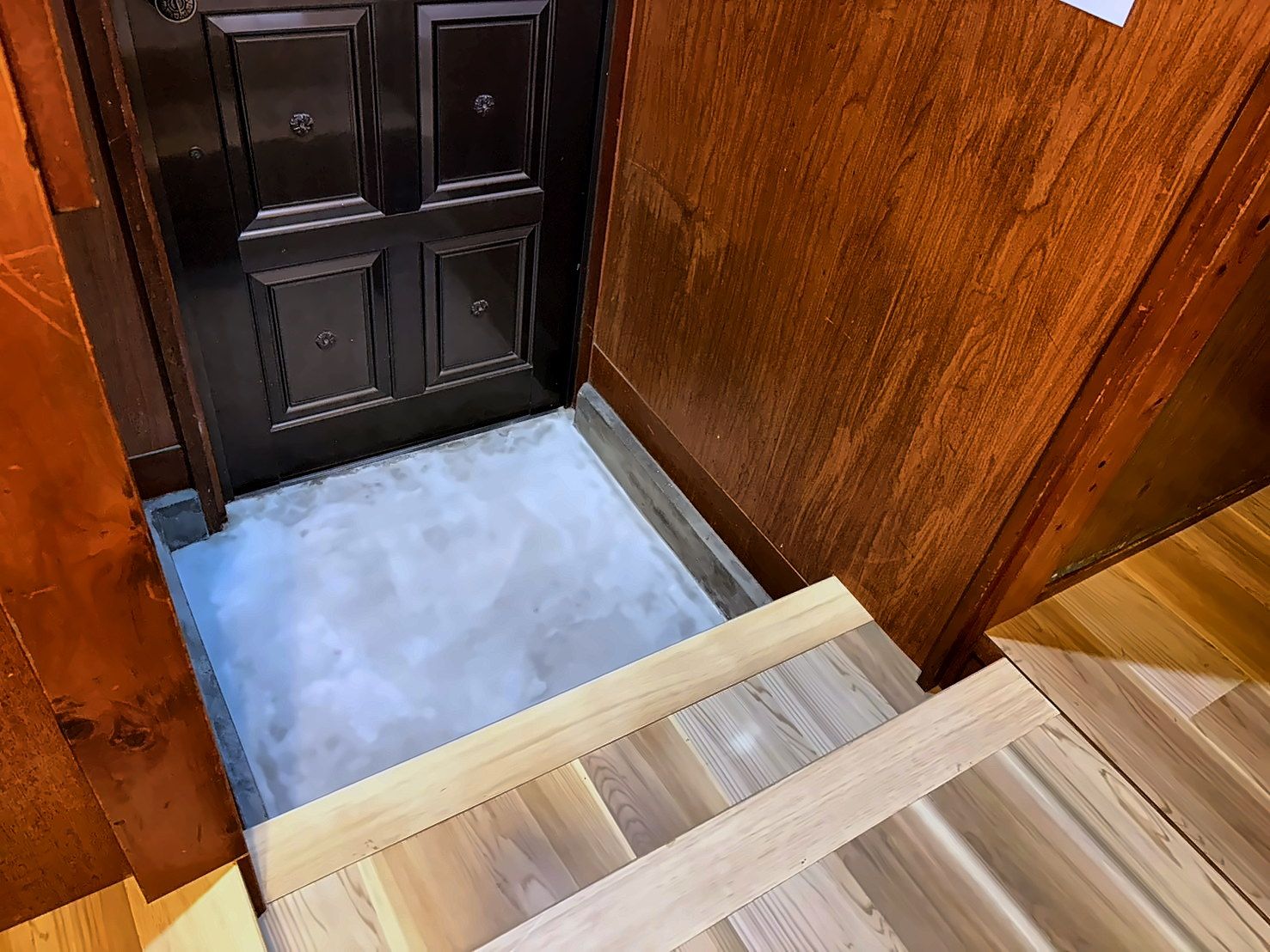 A wooden door with a small step leading to a tiled floor.